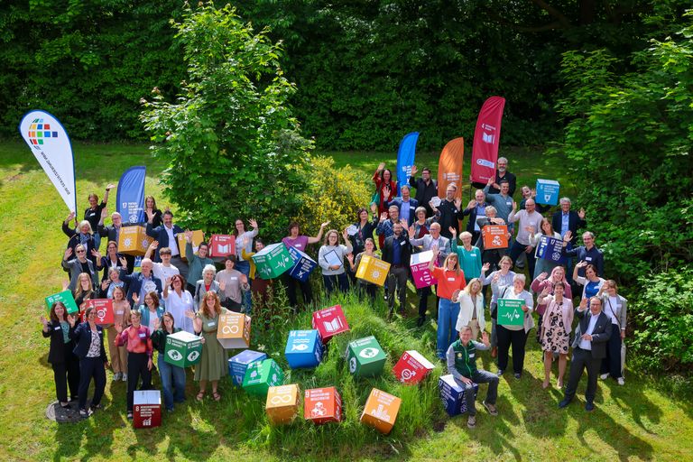Große Gruppe hält bunte Recyclingboxen in Wald, Umweltschutzaktion.
