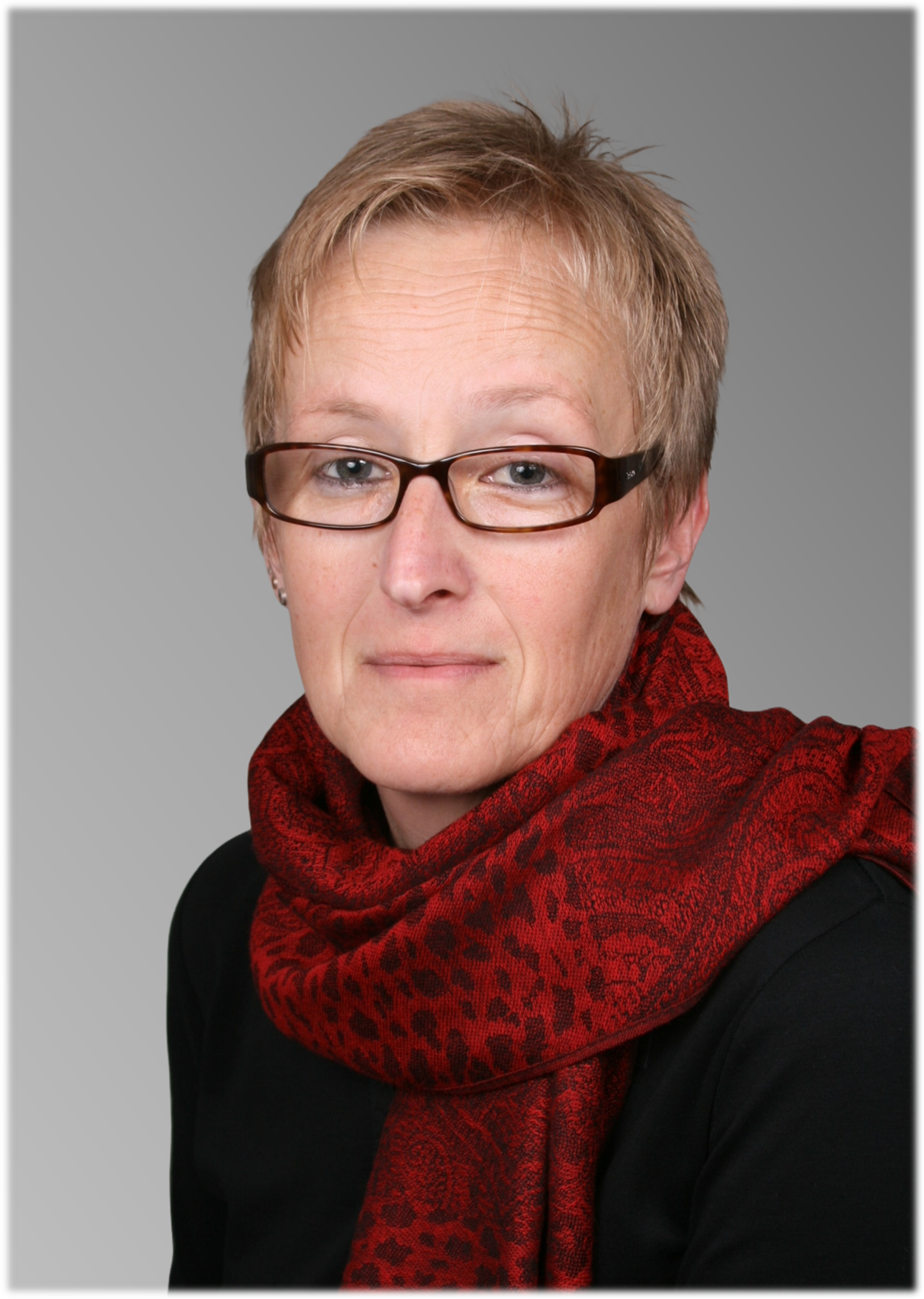 Porträt einer Frau mit Brille und rotem Schal vor hellem Hintergrund.