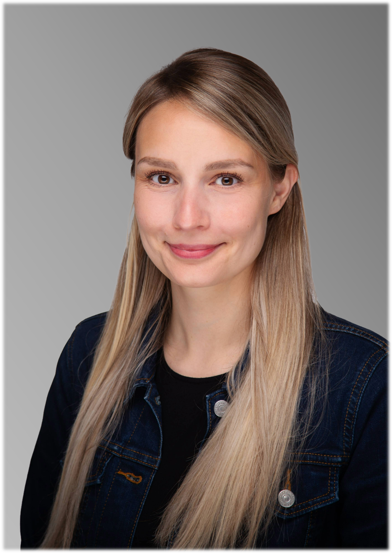 Frau mit blonden Haaren lächelt in dunkler Denim-Jacke über schwarzem Shirt.